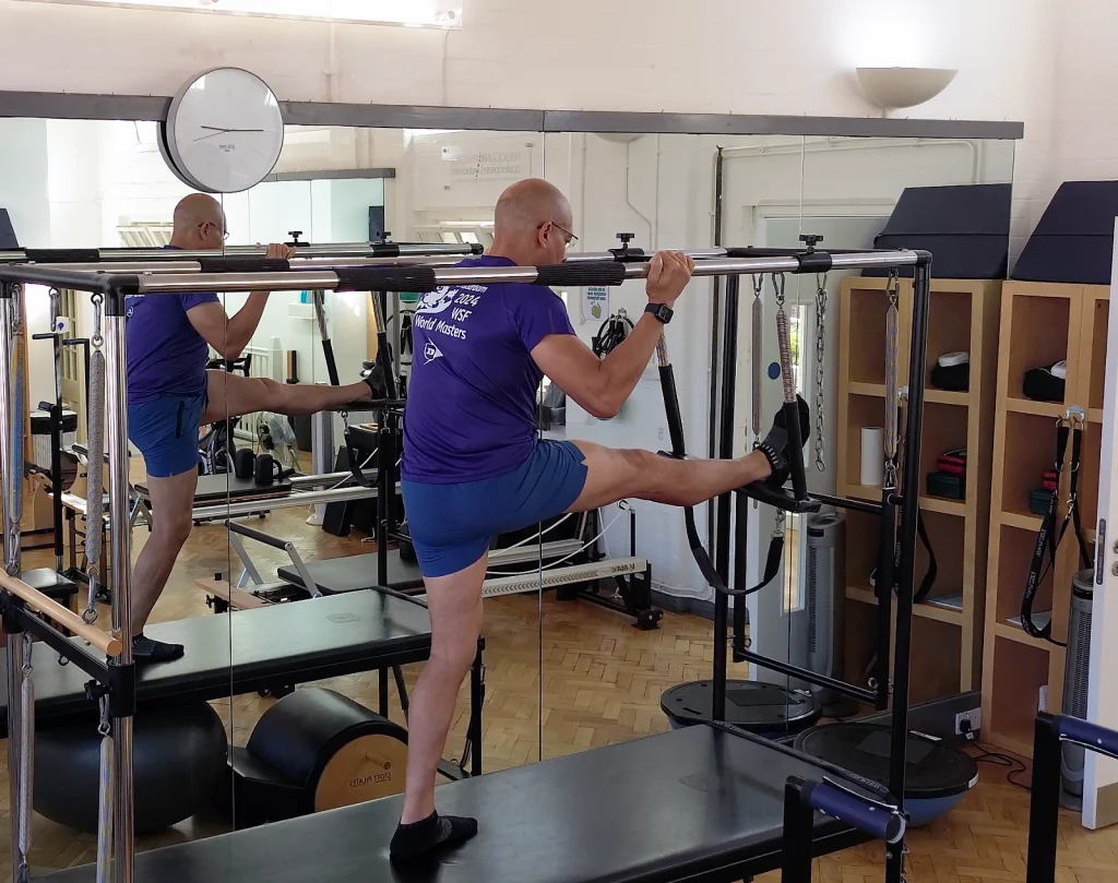 Teejay Sogunro using the Cadillac Trapeze Table for a supported standing hamstring stretch at Applied Pilates, London Colney, St Albans